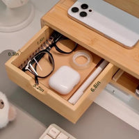 Belcrest natural bamboo monitor riser with drawer and open storage, holding glasses, earbuds, tape, and pen.