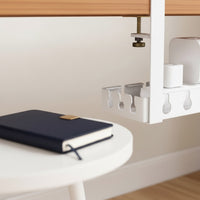 Belcrest white metal under desk cable management tray with adjustable width, holding white adapters and a notebook.